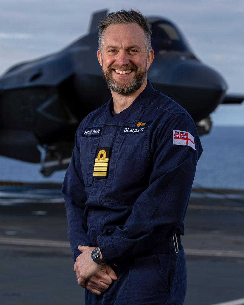 Captain Will Blackett in front of an F-35 on the flight deck of HMS Prince of Wales